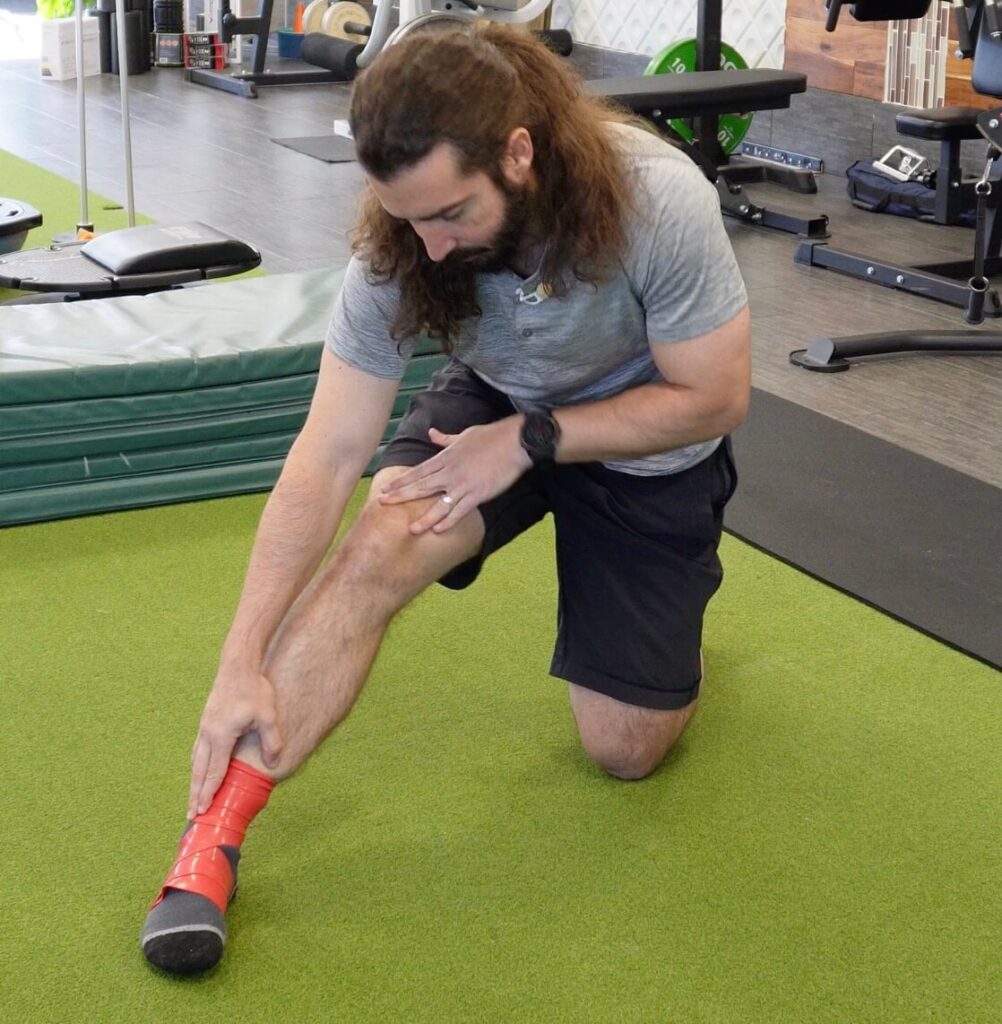 Dr. John demonstrating plantar flexion with a muscle band on as an ankle rehab exercise